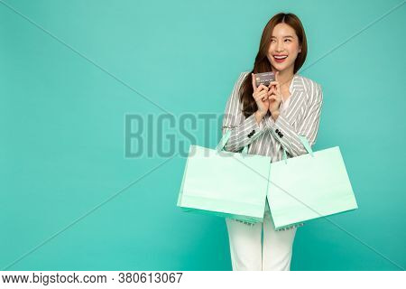 Portrait Of Smiling Asian Women Holding Credit Card And Green Shopping Bag Isolated Over Green Backg
