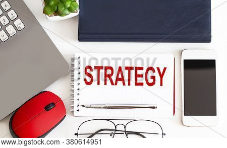 Laptop, Pen And Notepad With Text Strategy In The White Background With Office Tools