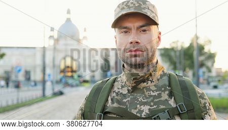 Portrait Of Serious Caucasian Handsome Young Male Soldier In Cap With Backpack Standing At Street. M