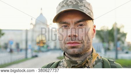 Portrait Of Serious Caucasian Handsome Young Male Soldier In Cap With Backpack Standing At Street. M