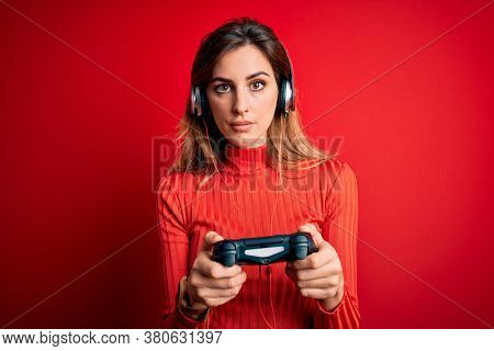 Young beautiful brunette gamer woman playing video game using joystic and headphones with a confident expression on smart face thinking serious