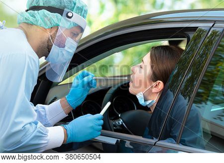 Woman getting tested at a coronavirus drive thru station by medical staff with PPE suit by throat swab. Health care drive thru service and medical concept