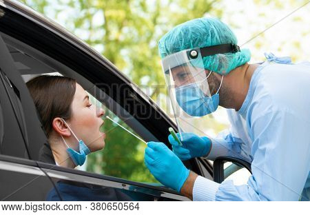 Woman getting tested at a coronavirus drive thru station by medical staff with PPE suit by throat swab. Health care drive thru service and medical concept