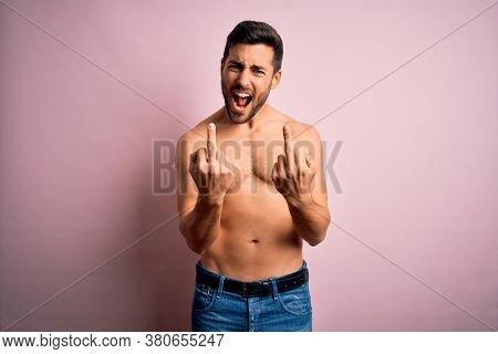 Young handsome strong man with beard shirtless standing over isolated pink background Showing middle finger doing fuck you bad expression, provocation and rude attitude. Screaming excited