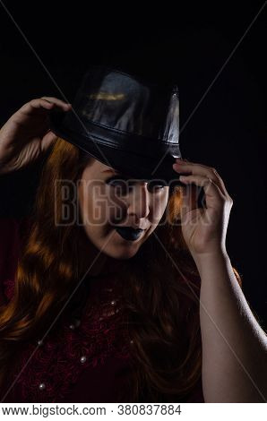Portrait Of A Beautiful Redhead With Hat Made In Studio, Low Key Image, With Black Background.