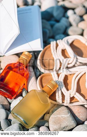 Beach Hat On Opened Book With Sunscreen And Shoes On Pebble Beach