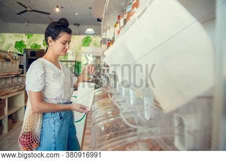 Young Woman Filling Up Reusable Bag With Pasta, Nuts Or Grains In Zero Waste Plastic Free Store. Low