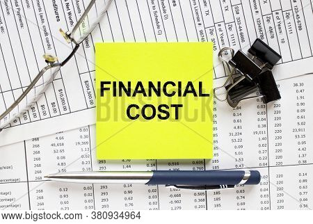 Text Financial Cost On Financial Tables With Pen, Glasses And Paper Clips