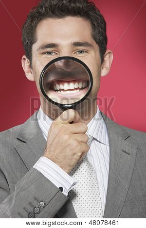 Closeup de um empresário segurando lupa sorrindo a boca contra o fundo vermelho