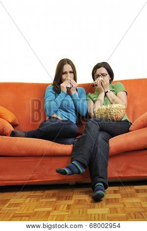 female friends eating popcorn and watching tv at home on orange sofa isolated on white