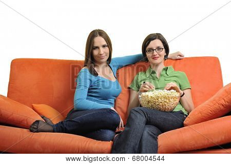 female friends eating popcorn and watching tv at home on orange sofa isolated on white