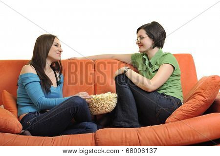 female friends eating popcorn and watching tv at home on orange sofa isolated on white