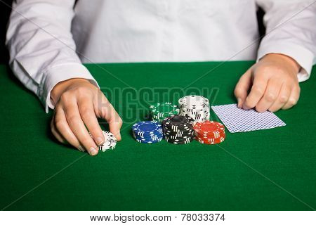 casino, gambling, poker, people and entertainment concept - close up of holdem dealer with playing cards and chips on green table