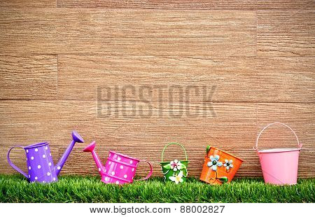 watering cans and pails on green grass with wood background