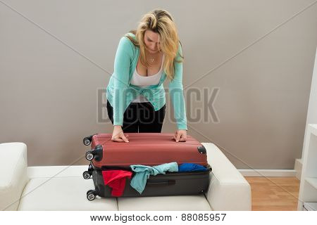 Woman Trying To Close The Suitcase