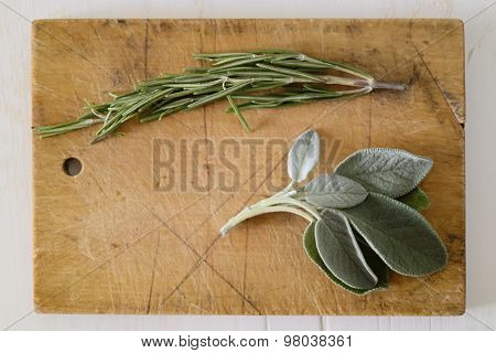 Two Fresh Green Mediterranean Herbs Rosemary Branch And Sage Leaves On A Brown Wood Cutting Board On
