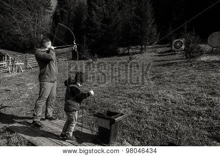The father teaches his son to shoot a bow