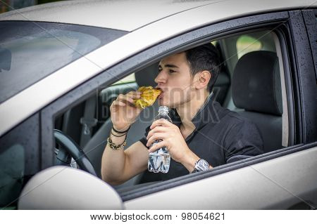 Young man driving his car while eating food