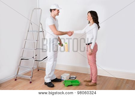 Woman Shaking Hands To Painter With Paint Roller At Home