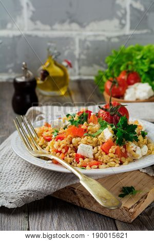 Tabula. Bulgur with baked pepper tomato and feta cheese on an old wooden background. Selective focus.