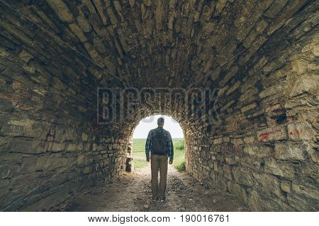 man stands in old castle tunnel with light in the end