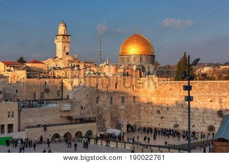 Sunset view of Temple Mount in the old city of Jerusalem, including the Western Wall and golden Dome of the Rock, packed with people - pilgrims and tourists.