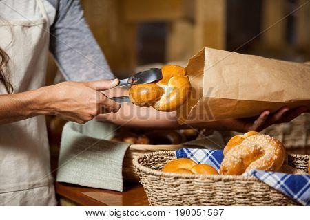 Mid-section of staff packing bread in paper bag at bakery shop