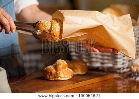 Mid-section of female staff packing sweet food in paper bag at supermarket
