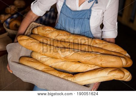 Mid-section of female staff holding basket of baguettes in bakery section of supermarket