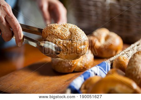 Hands of female staff holding sweet food with tongs in supermarket