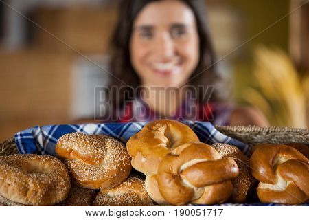 Smiling female staff holding wicker basket of various breads at counter in bakery shop