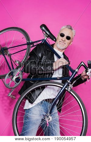 Cheerful Senior Man Wearing Leather Jacket And Sunglesses Holding Bicycle On His Shoulders Isolated
