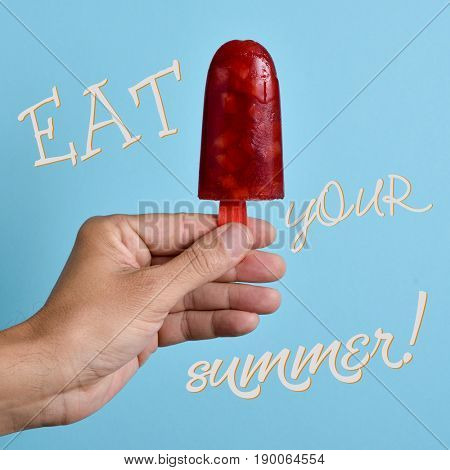 the text eat your summer and a homemade natural ice pop in the hand of a young caucasian man, against a bright blue background
