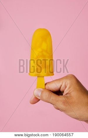 closeup of a young caucasian man with a homemade natural ice pop in his hand, against a pink background