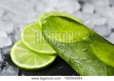 closeup of a homemade mojito ice pop made with natural lime juice, rum, mint and lime slices, on a natural slate tray surrounded by ice