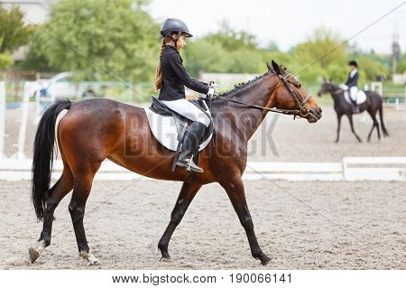Young teenage girl in helmet riding horse on dressage equestrian competition