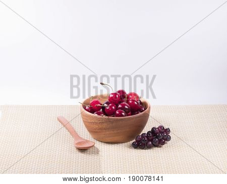 Cherries in wooden bowl and wooden spoon dark grapes flower with white background