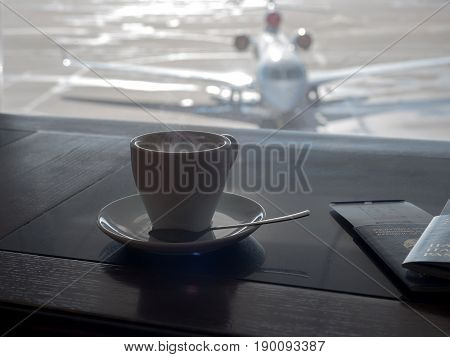 Cup of coffee in airport's business lounge with aircraft.