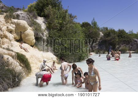 BAGNO VIGNONI, ITALY - JUNE 3 2017: People bathing in the free area of Bagno Vignoni in Tuscany Italy free accessible hot springs puddle trough vegetation