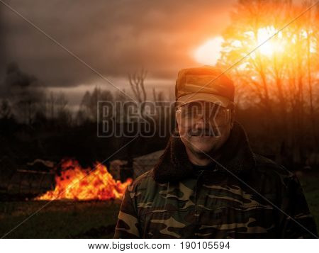 A man in uniform armed with a fire. Smile of the prankster. In the background, the building burns.