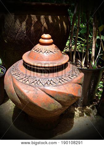 earthen jar in a garden
A big earthen jar with decorative designs and cover placed in a garden