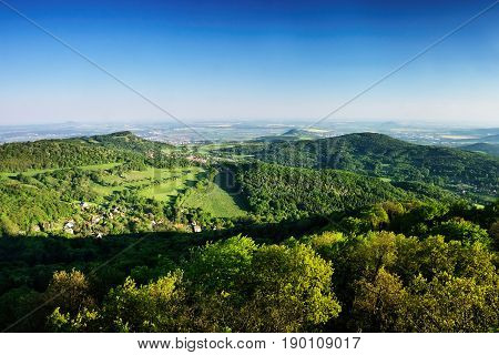 Ceske Stredohori tourist area with hill Kamyk and Litomerice city on horizont and Kundratice village in foreground in spring evening czech landscape during sunset