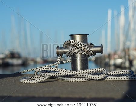Stainless steel bollard with rope in a luxury marina soft bokeh with luxury boats and yachts