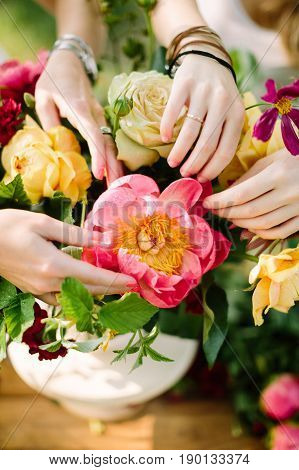 applied art, wedding, floral design, accessoiries, summer, nature concept - beautiful women's hands with rings and bracelets making bouquet of creamy roses, coral peony and bright red dianthuses