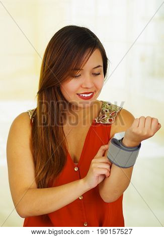 Beautiful young patient using an automatic tensiometer in her arm, in a doctor consulting room background.