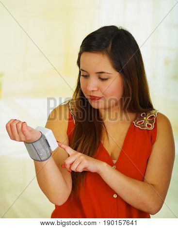 Beautiful young patient using an automatic tensiometer in her arm, in a doctor consulting room background.