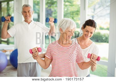 Female trainer assisting senior couple in performing exercise at home