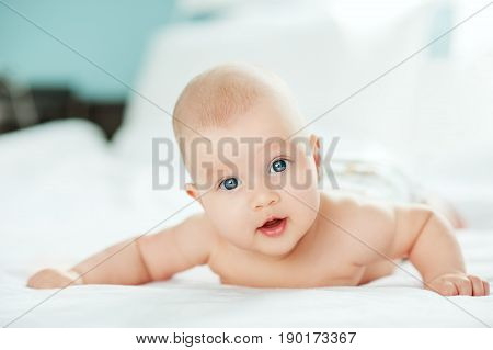 Adorable baby girl in white sunny bedroom. Newborn child relaxing and laying on belly on bed. Nursery for young children. Textile for kids. Family morning at home. Newborn kid during tummy time.