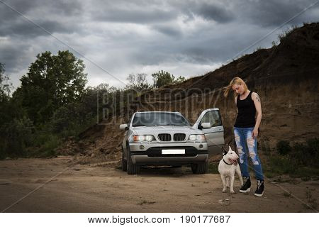 Brutal, daring girl with a fighting dog breed of bull terrier, near his car against the background of the rock