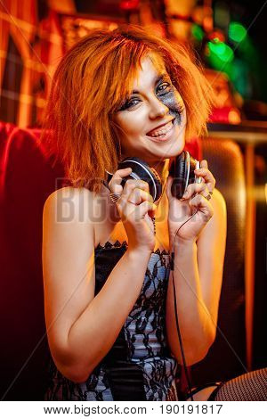 Redhaired girl in headphones with unusual makeup at the disco